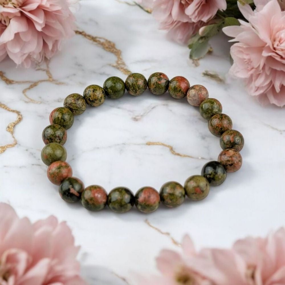 Unakite bracelet for pregnancy support on a marble surface with pink flowers