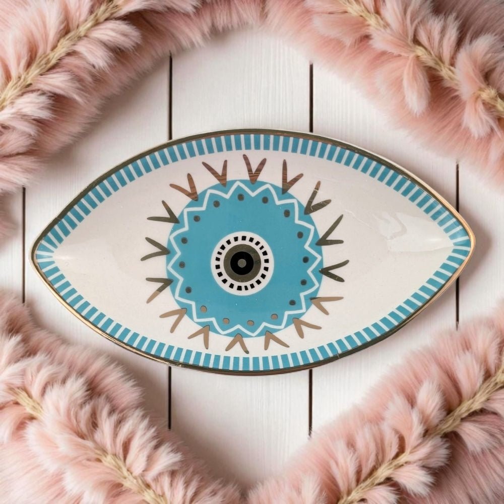 Decorative plate with eye design on a white wooden surface with pink feathers