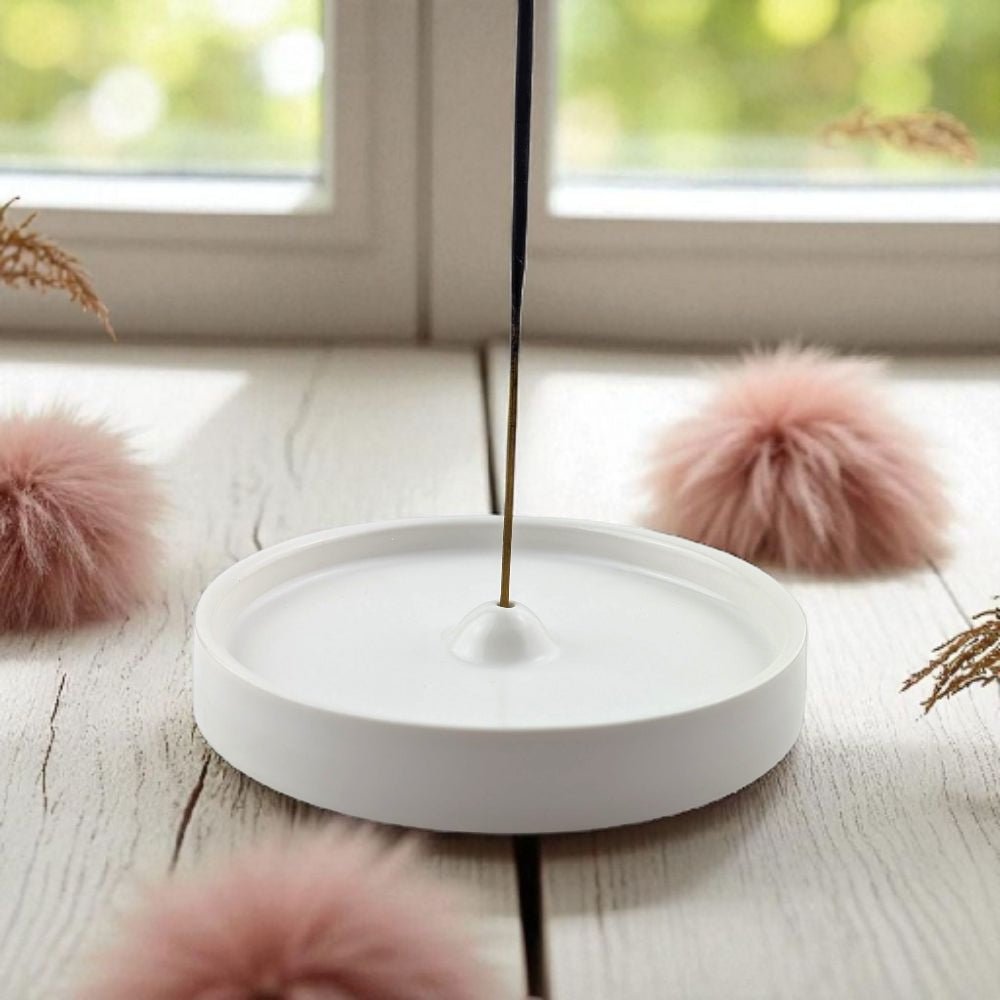 Incense stick burning in a white holder with pink decorative elements on a wooden surface.