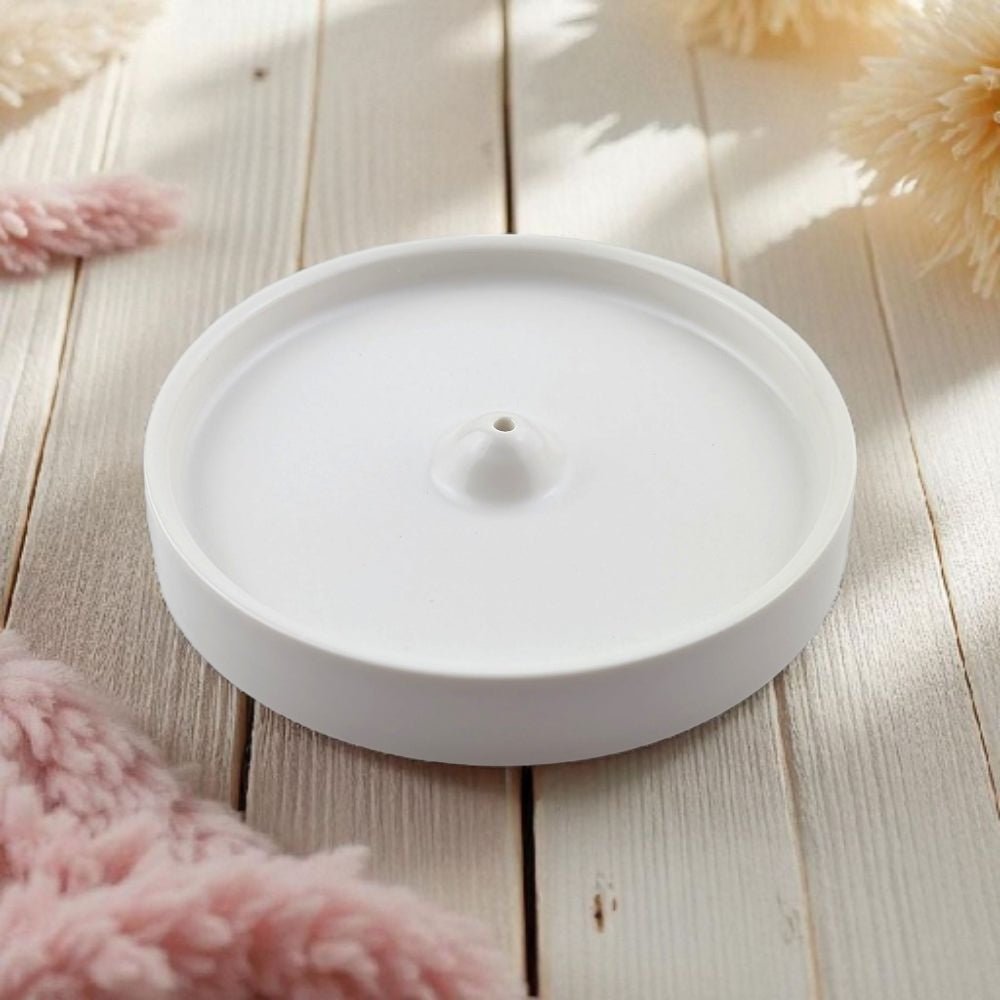 White ceramic incense burner on a wooden surface with soft pink flowers in the background