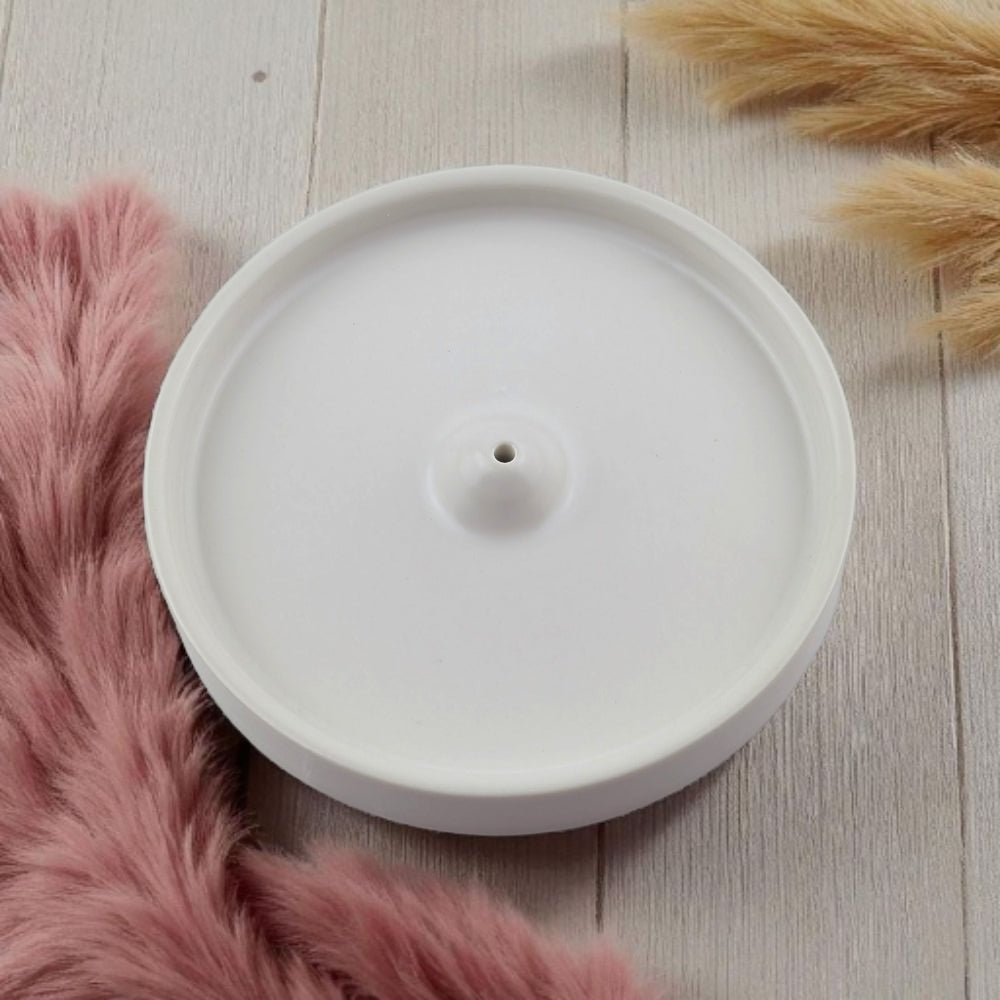 White ceramic incense burner on a wooden surface with pink fur and dried plants
