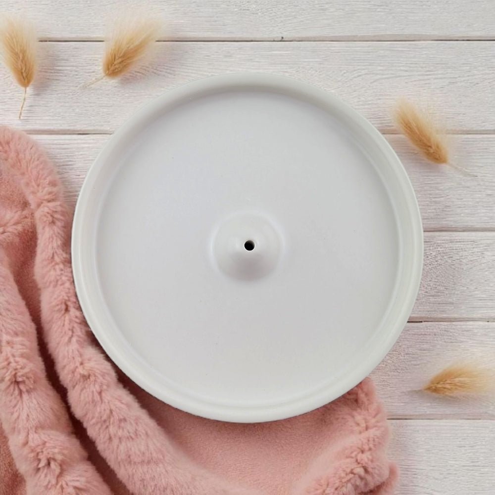 White ceramic incense burner on a pink textured fabric with dried plants on a light wooden surface