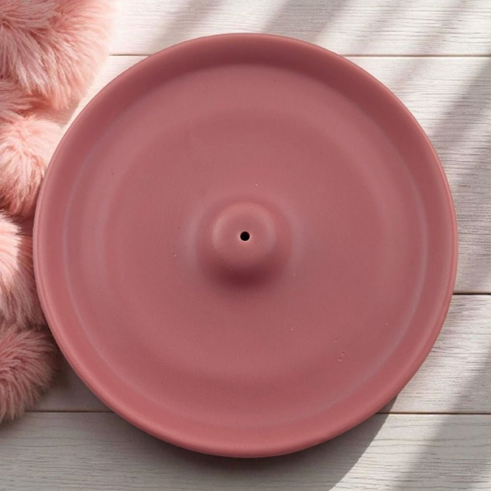 Pink ceramic incense burner on a light wooden surface with a fluffy pink object beside it.
