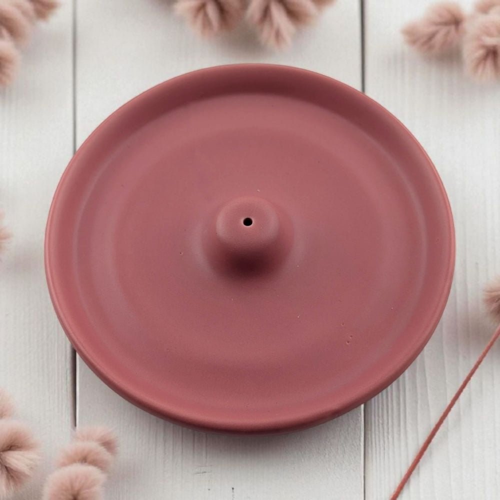 Pink ceramic modern incense burner on a light wooden surface with pink decorative elements.