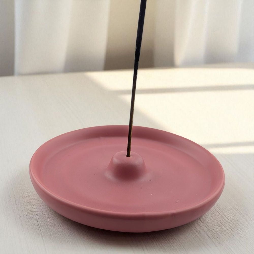 Pink incense burner with a single stick of incense on a light surface.