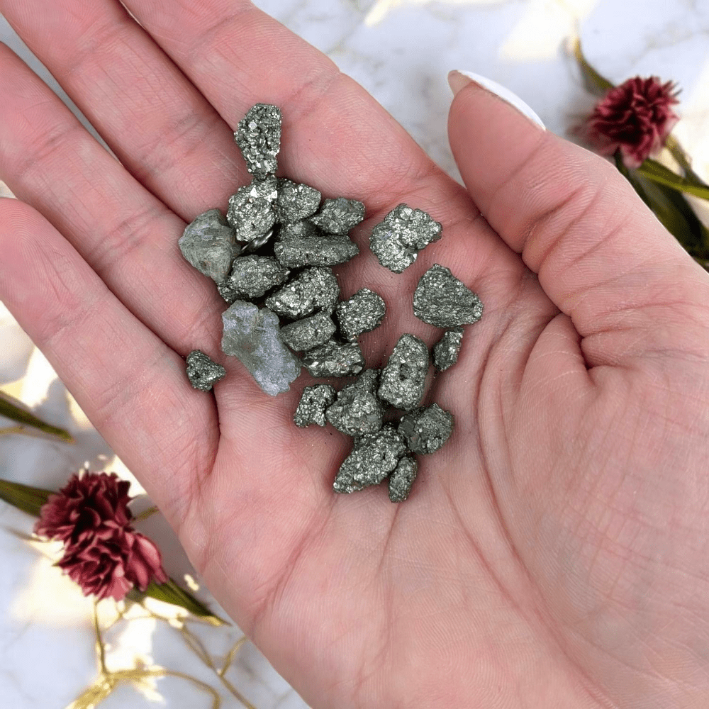 Hand holding small metallic pyrite rocks with a blurred decorative background