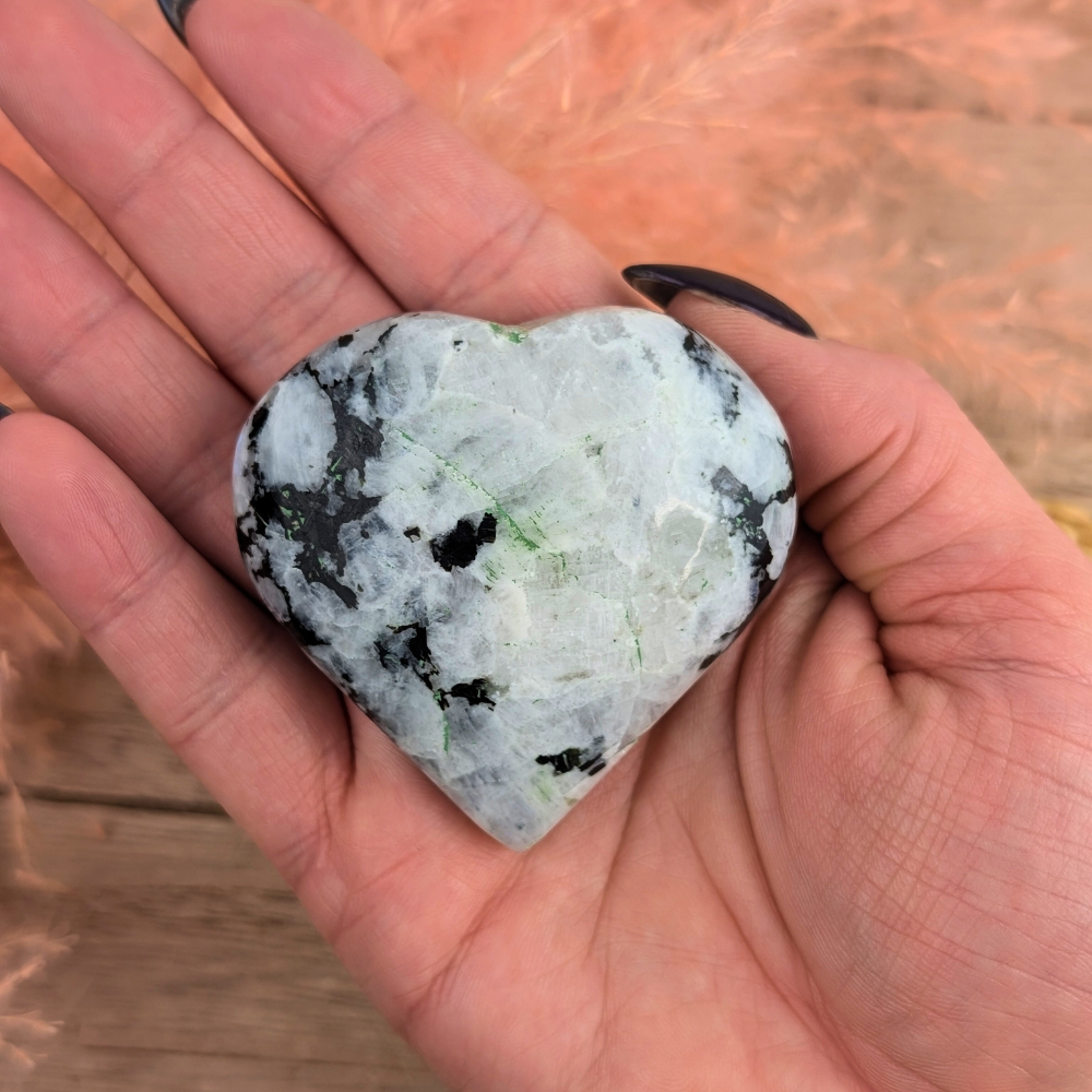 Smooth Rainbow Moonstone Crystal Heart lying flat on a wooden surface