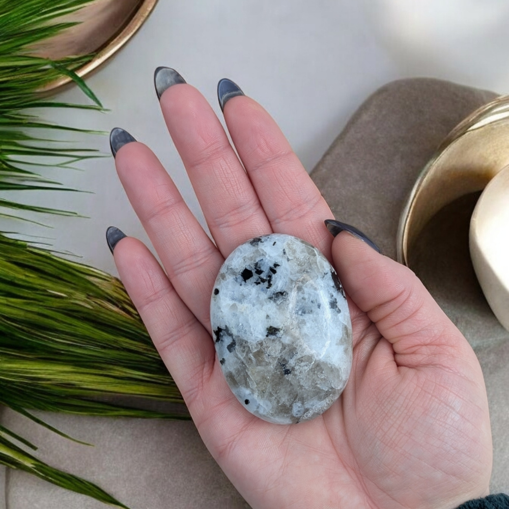 Rainbow Moonstone Palm Stone resting on an altar with greenery.