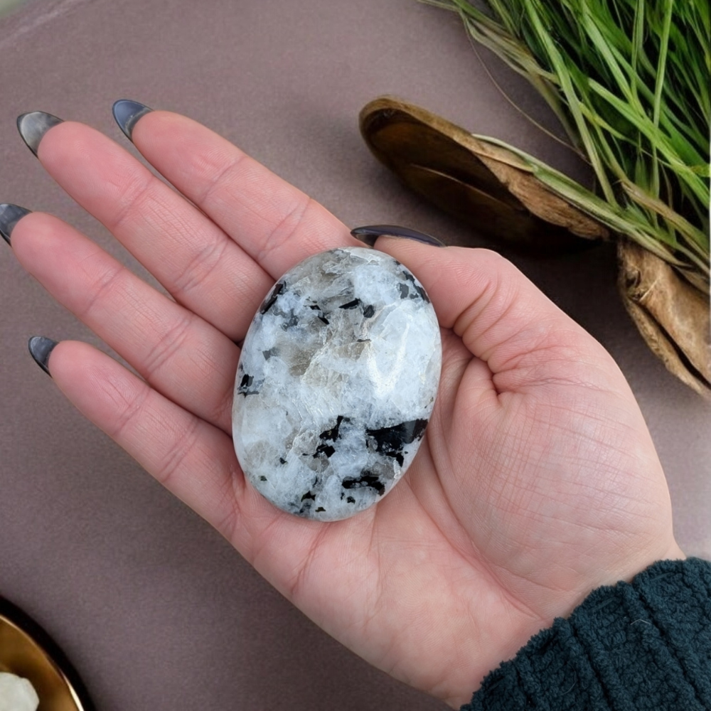 Hand holding Rainbow Moonstone Palm Stone for moon energy connection.