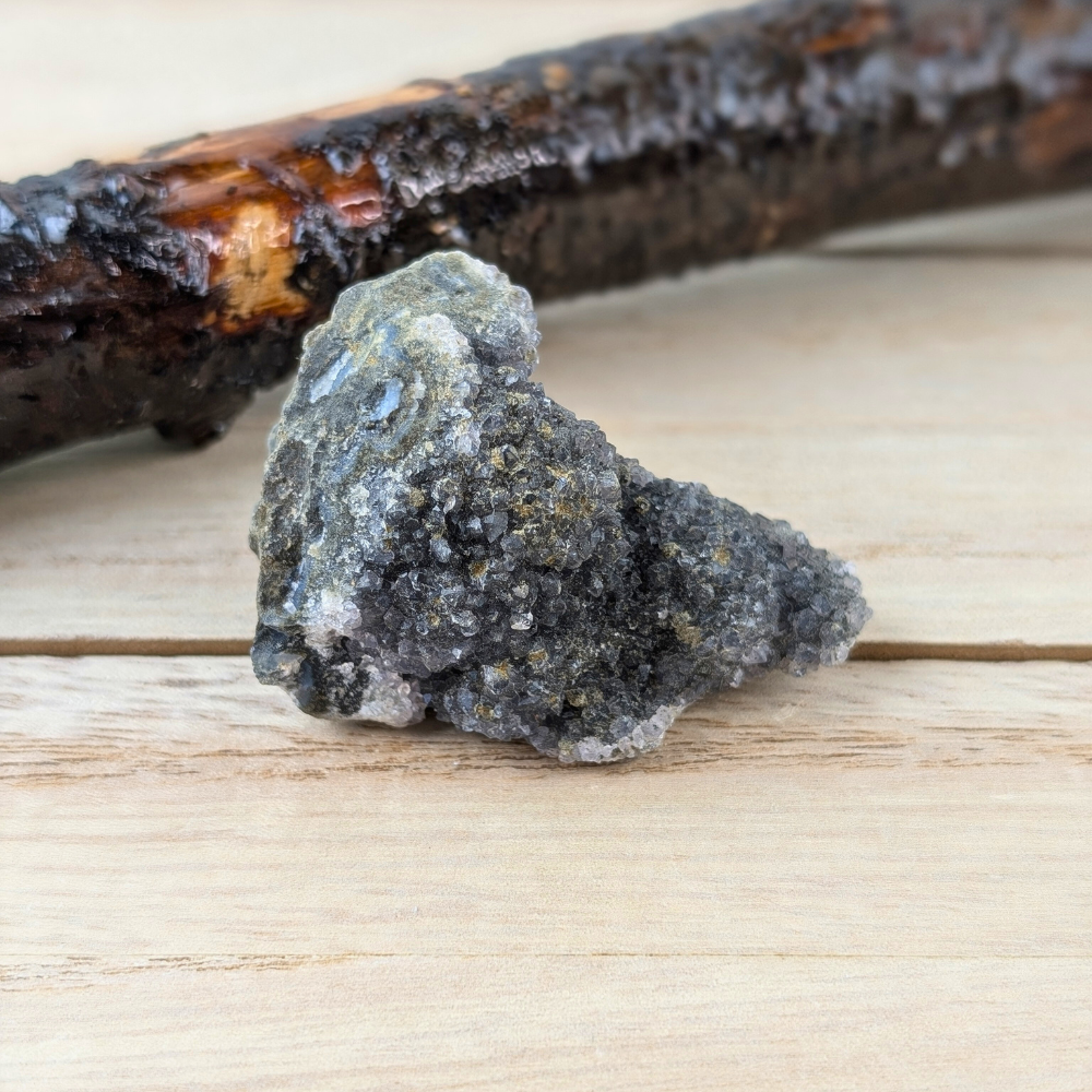 Compact Raw Rainbow Amethyst cluster on a natural wooden surface.