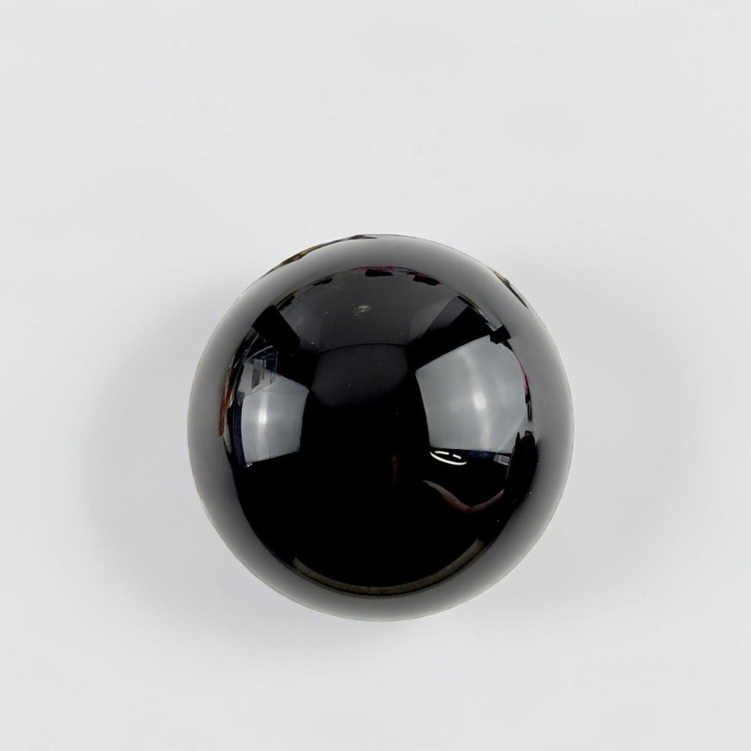 Root Chakra Black Obsidian Crystal Sphere on a stand with flowers and candles in the background available at zen collection metaphysical supply store