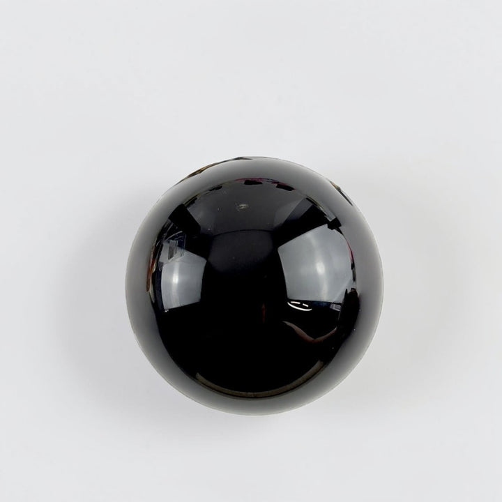 Root Chakra Black Obsidian Crystal Sphere on a stand with flowers and candles in the background available at zen collection metaphysical supply store