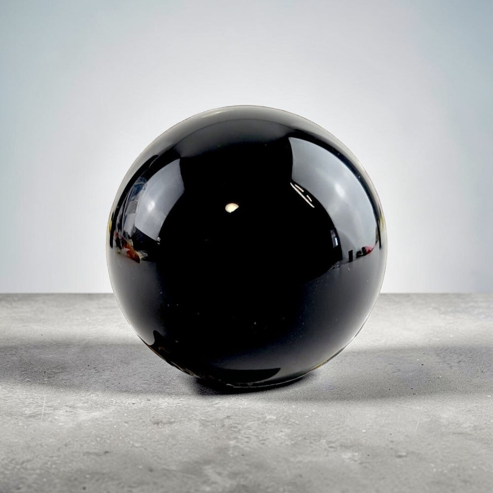 Root Chakra Black Obsidian  Crystal ball on a decorative stand with candles and roses in the background available at Zen Collection metaphysical supply store