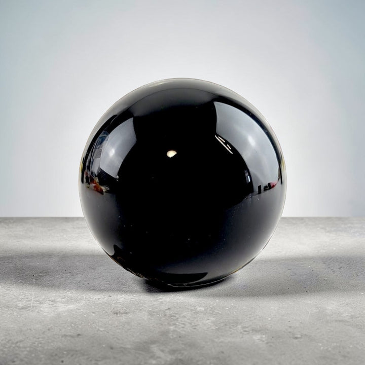 Root Chakra Black Obsidian  Crystal ball on a decorative stand with candles and roses in the background available at Zen Collection metaphysical supply store