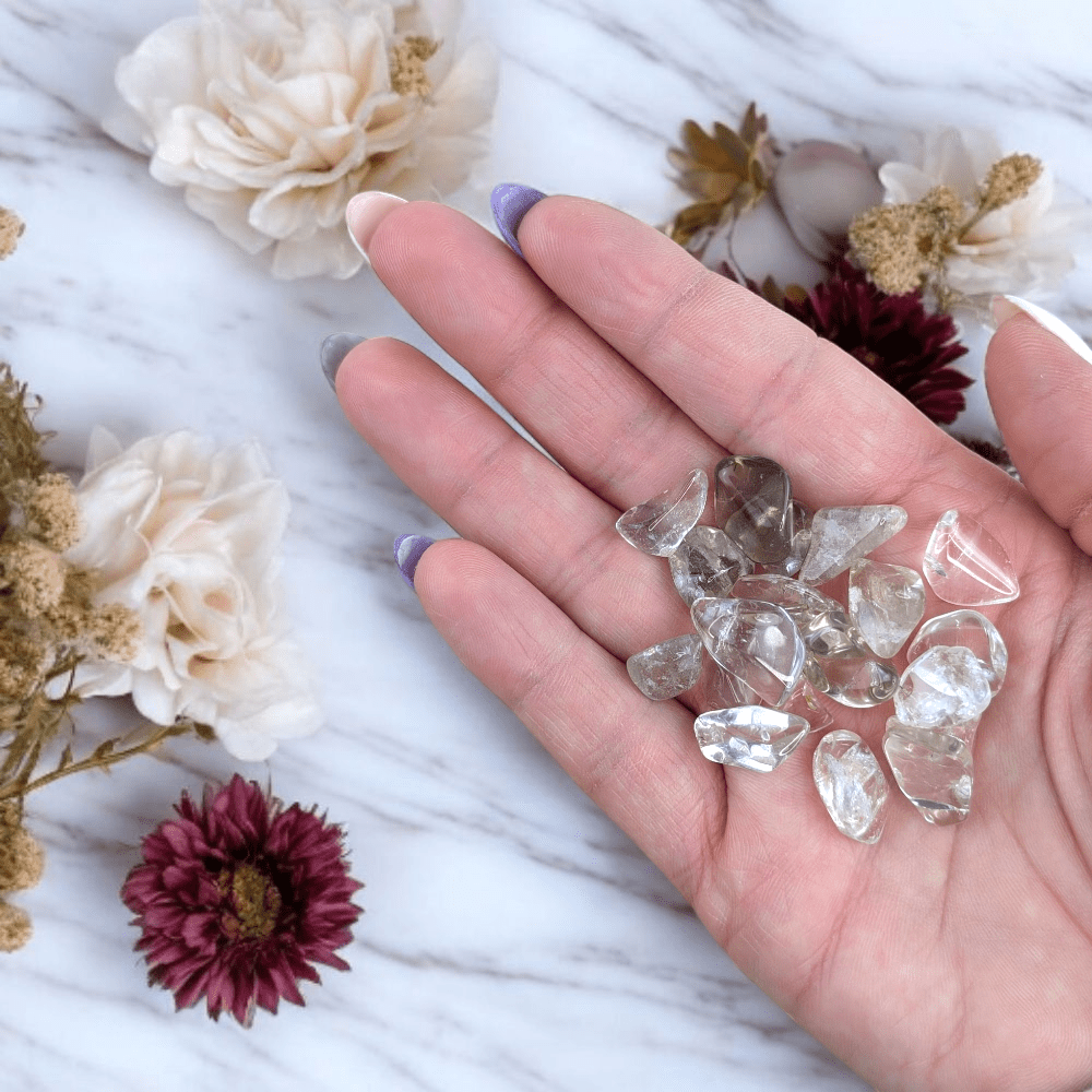 Hand holding smoky quartz crystals with flowers on a marble surface