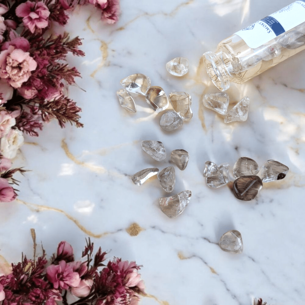 smoky quartz stones on a marble surface with pink flowers and a bottle cap.
