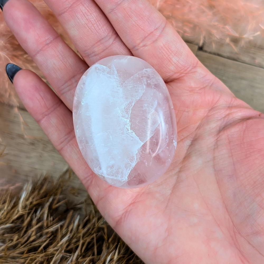 Rose Quartz Palm Stone on a wooden surface with soft lighting