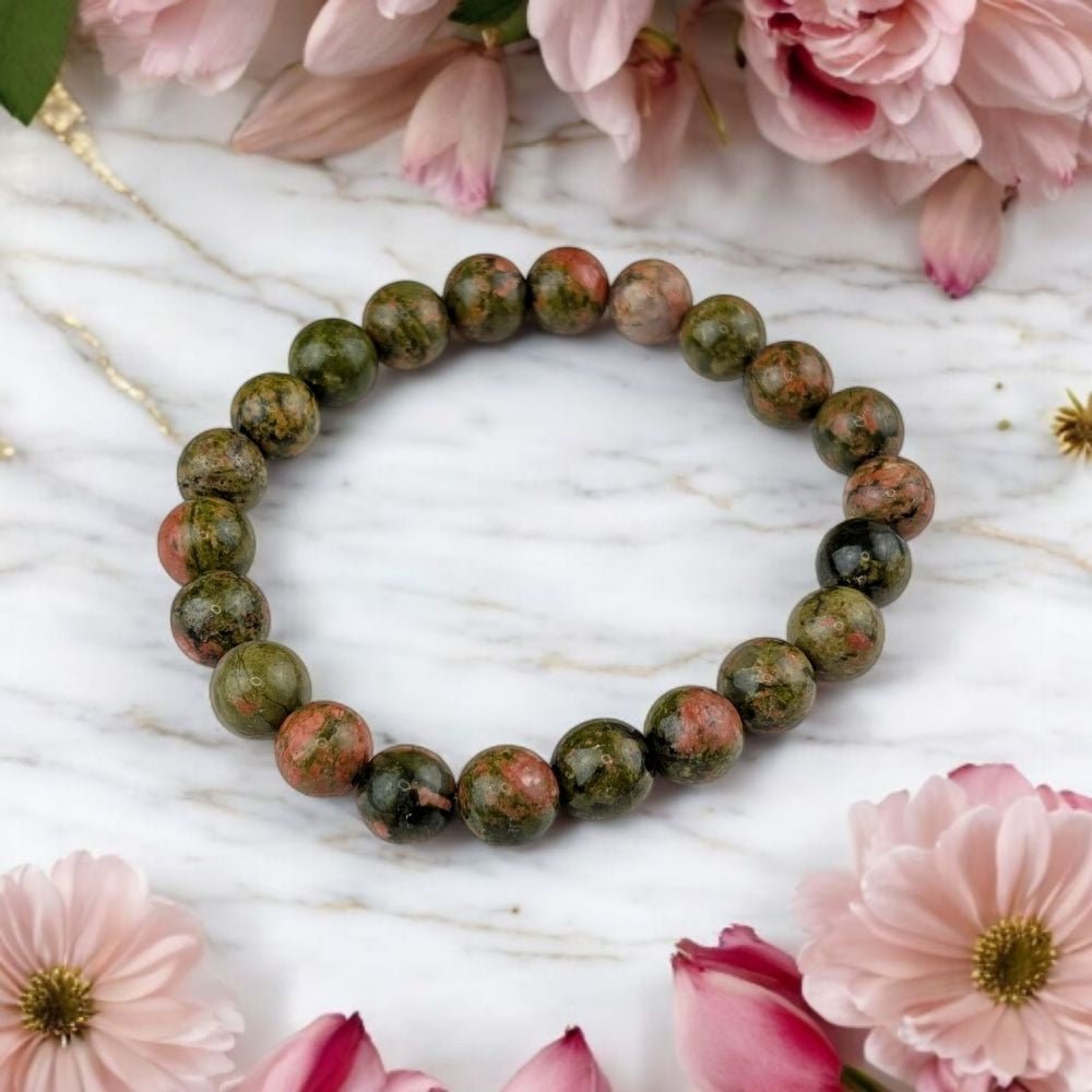 Green beaded bracelet on a marble surface with pink flowers