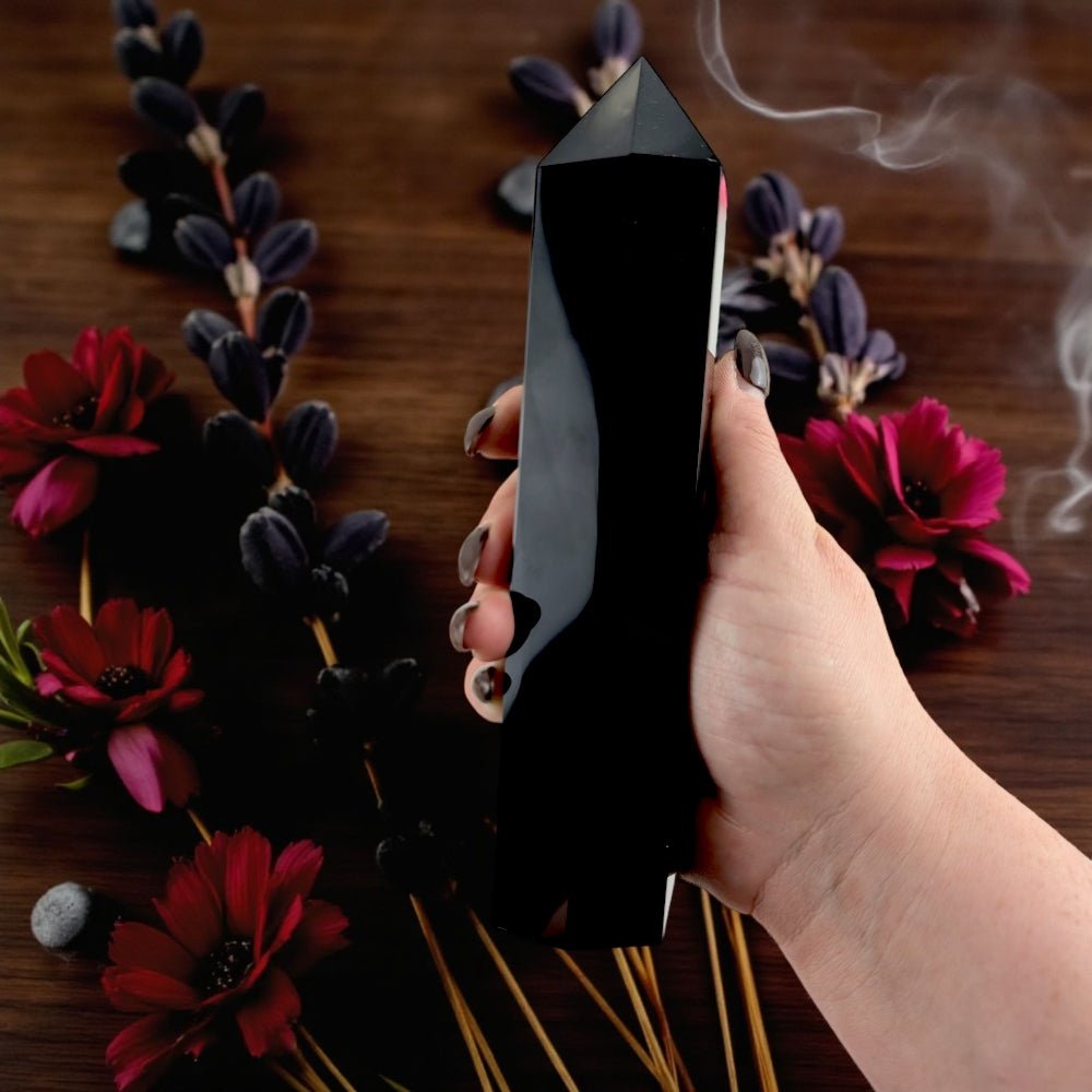 Hand holding a black Obsidian crystal tower with flowers and smoke on a wooden surface available at zen collection crystal store near you 