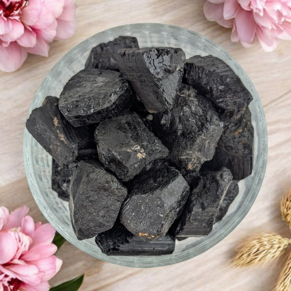 A person's hand holding various sizes of raw black tourmaline crystals.