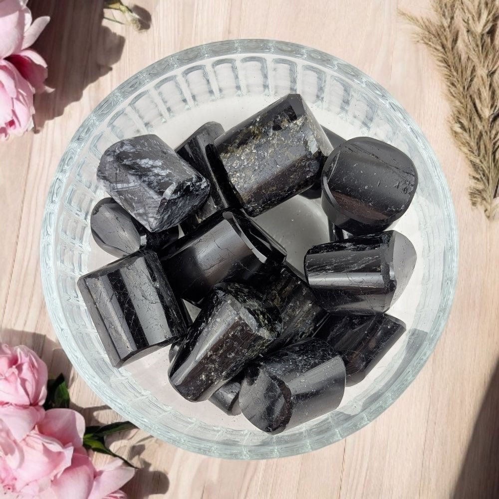 Black  Tourmaline stones in a glass bowl on a wooden surface with pink flowers
