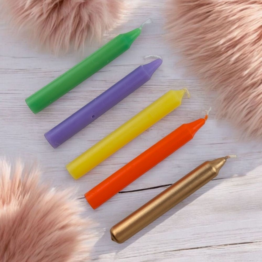 Five colorful chime candles (green, purple, yellow, orange, gold) on a light wooden surface with pink fur accents.