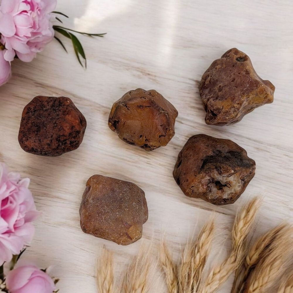 Five carnelian  crystals on a light wooden surface with pink flowers and dried wheat stalks.