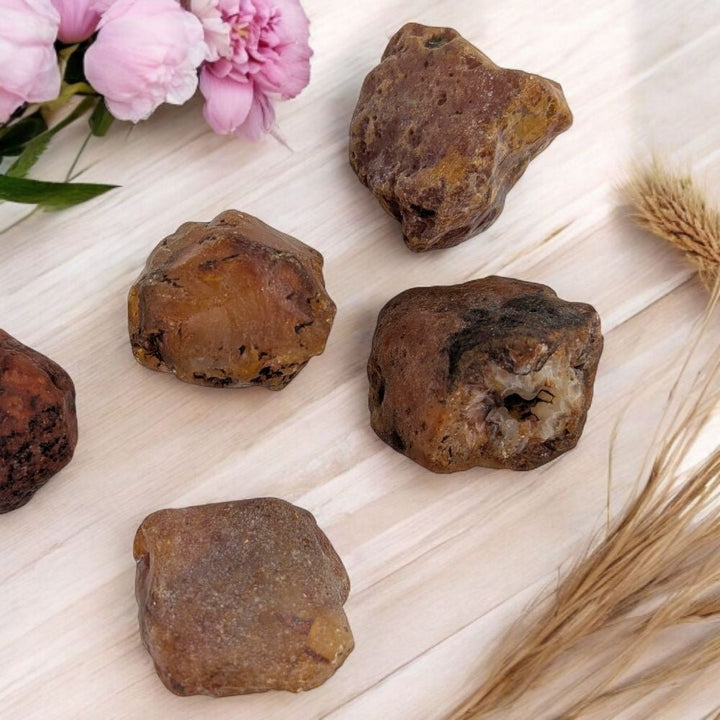 Raw carnelian stones on a light wooden surface with pink flowers and wheat stalks.