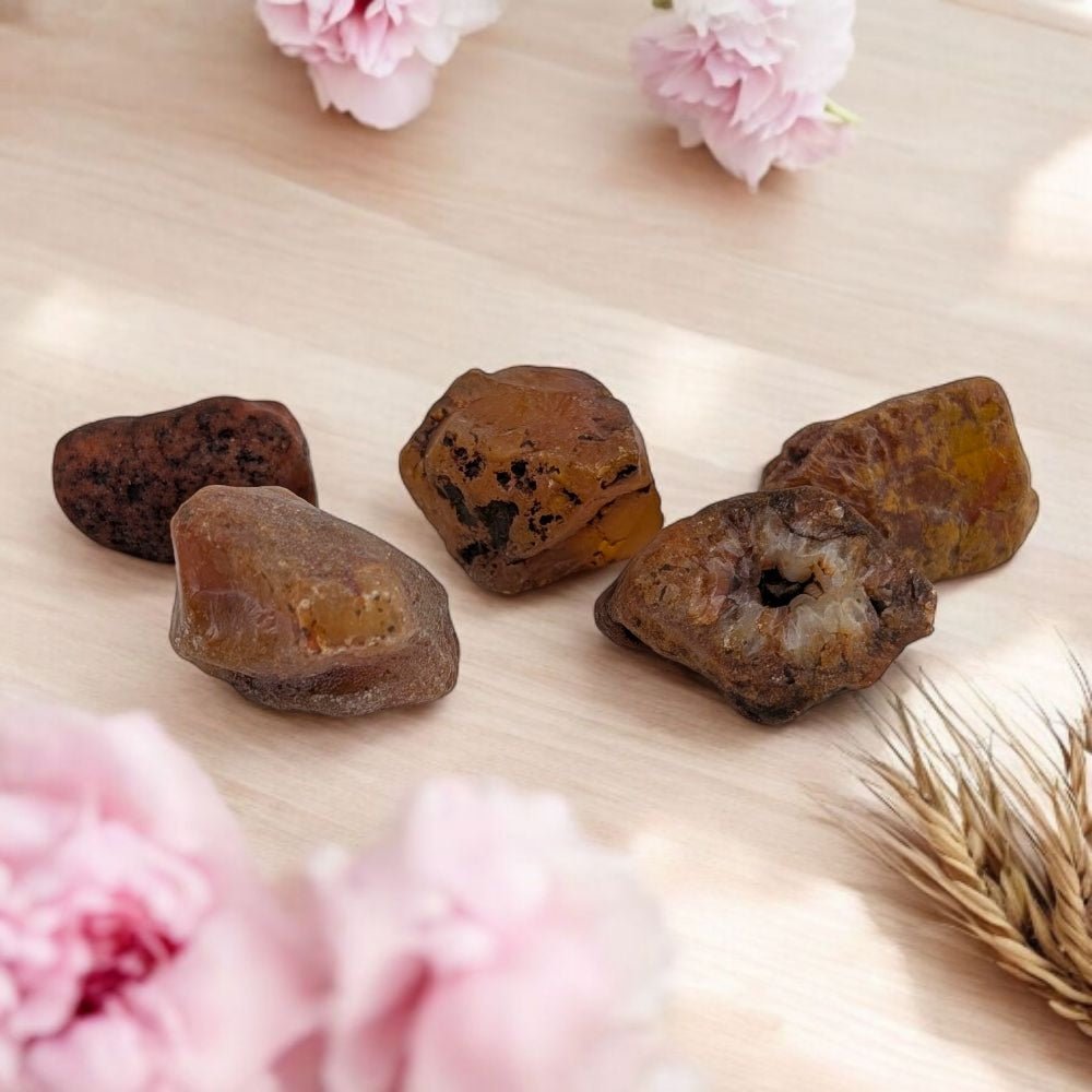 carnelian rocks on a light wooden surface with pink flowers and dried plants.