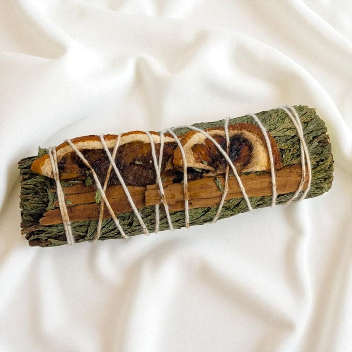 Rolled sage bundle with twine on a white fabric background available at zen collection crystal store in barrie ontario