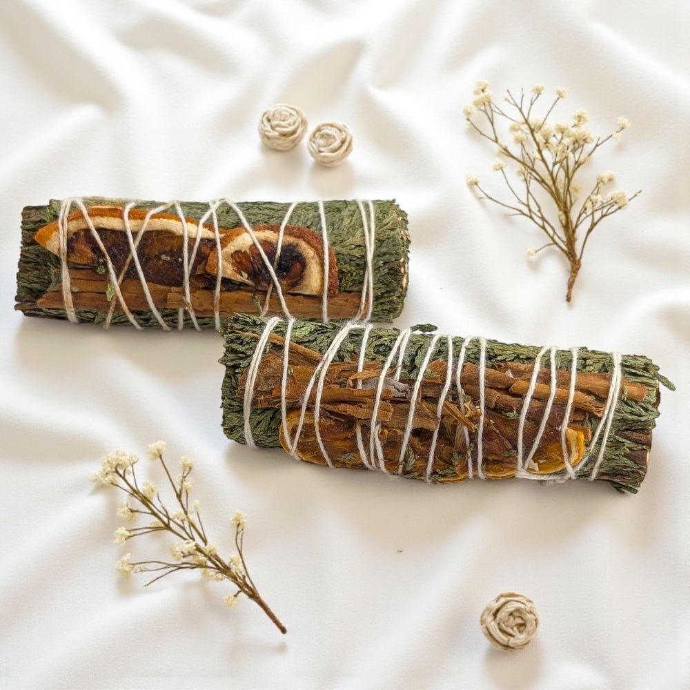 Two bundles of cedar and cinnamon sticks tied with twine on a white fabric background with small flowers. available at zen collection metaphysical  store in barrie