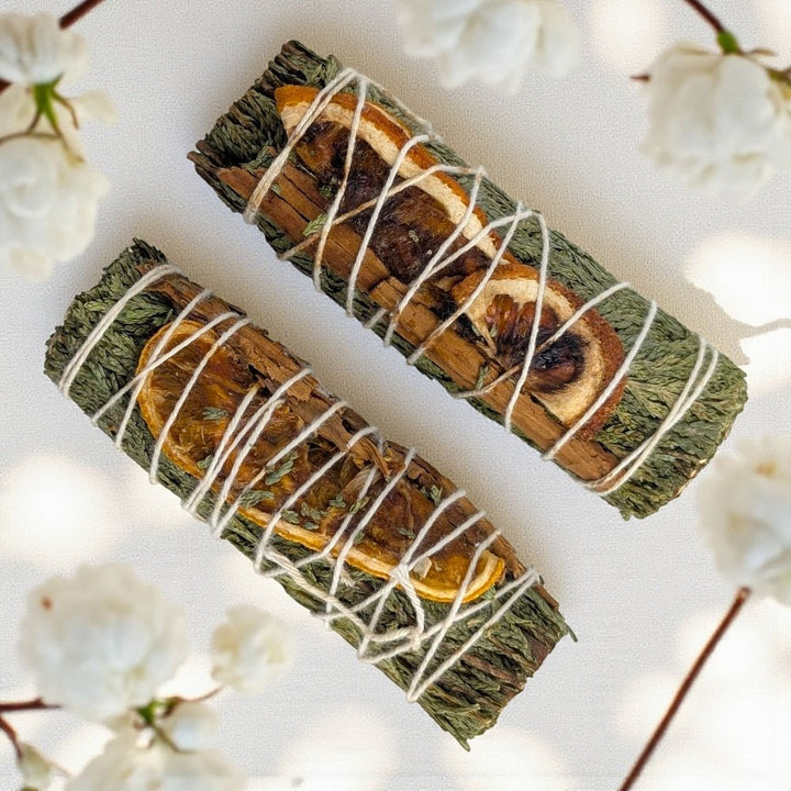 Two sage smudge sticks tied with string on a white background with blurred flowers. sourced from zen collection metaphysical store in Barrie Ontario