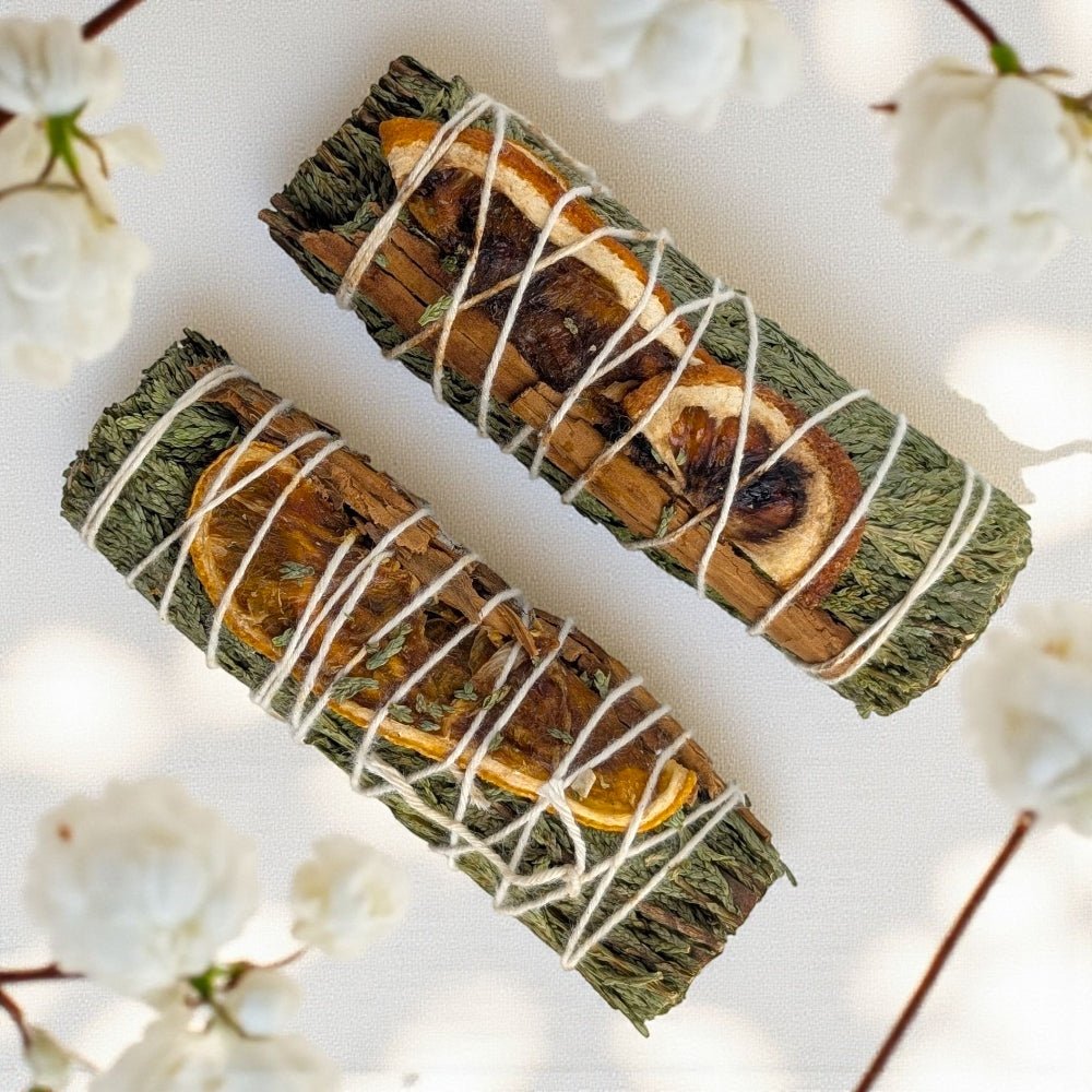 Two sage smudge sticks tied with string on a white background with blurred flowers. sourced from zen collection metaphysical store in Barrie Ontario