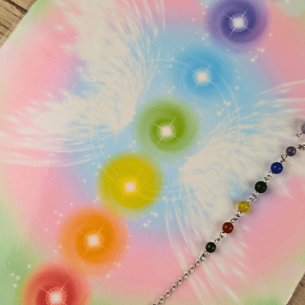 A colorful pendulum board with chakra symbols in green, orange, yellow, blue, indigo, and purple, against a white and pastel background. Available at Zen Collection Metaphysical Store in Barrie