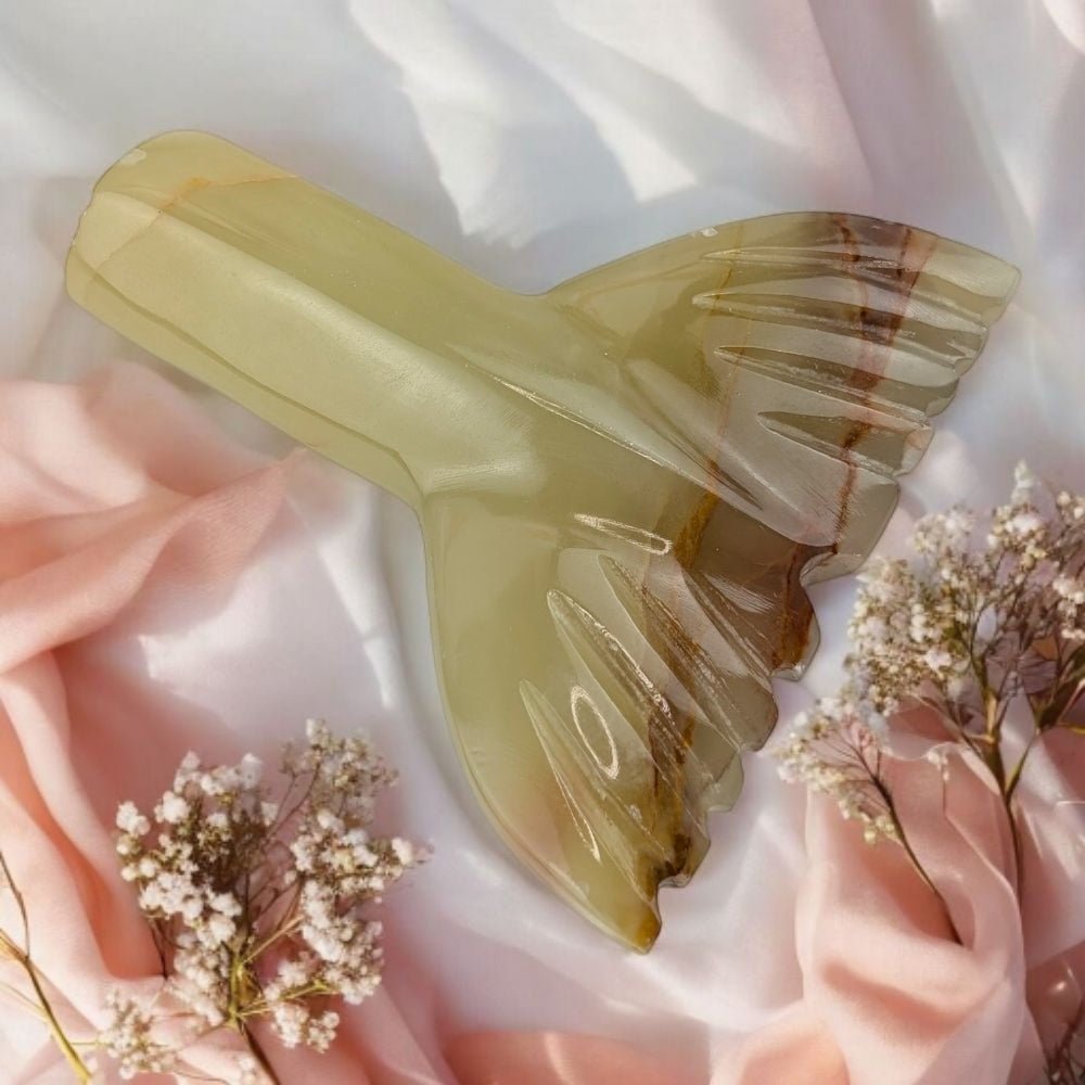 Decorative mermaid-shaped object on a soft pink fabric background with small white flowers.