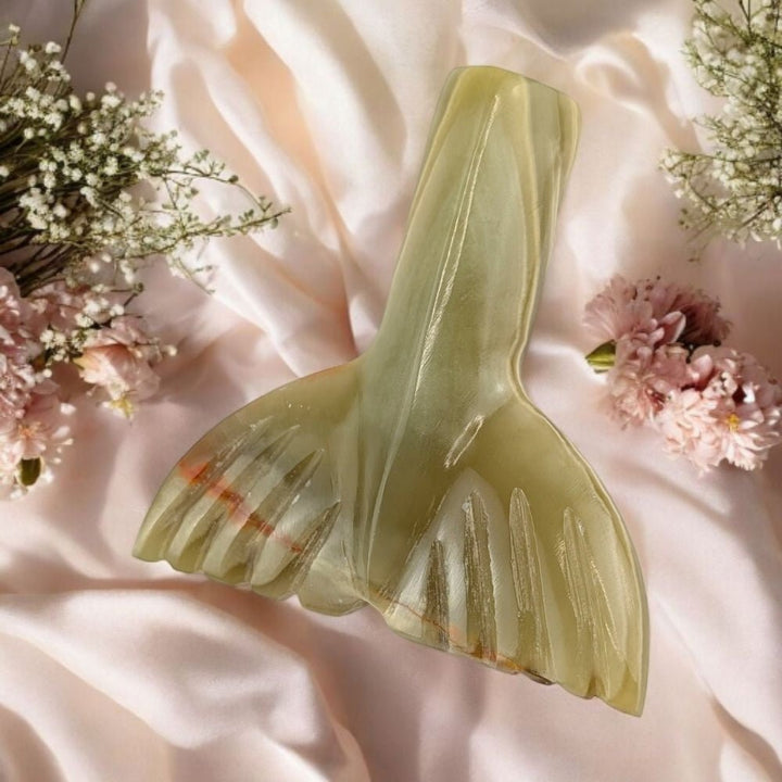 Decorative green crystal mermaid tail on a soft pink fabric background with flowers.