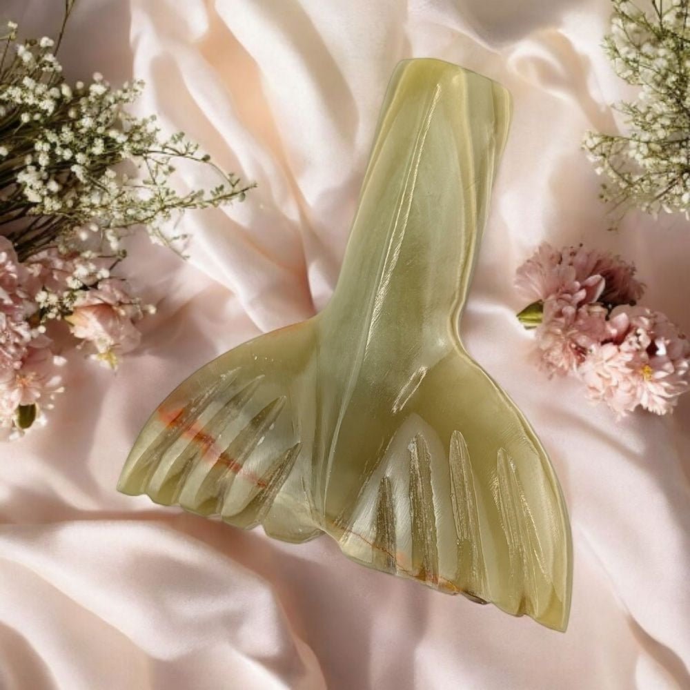 Decorative green crystal mermaid tail on a soft pink fabric background with flowers.