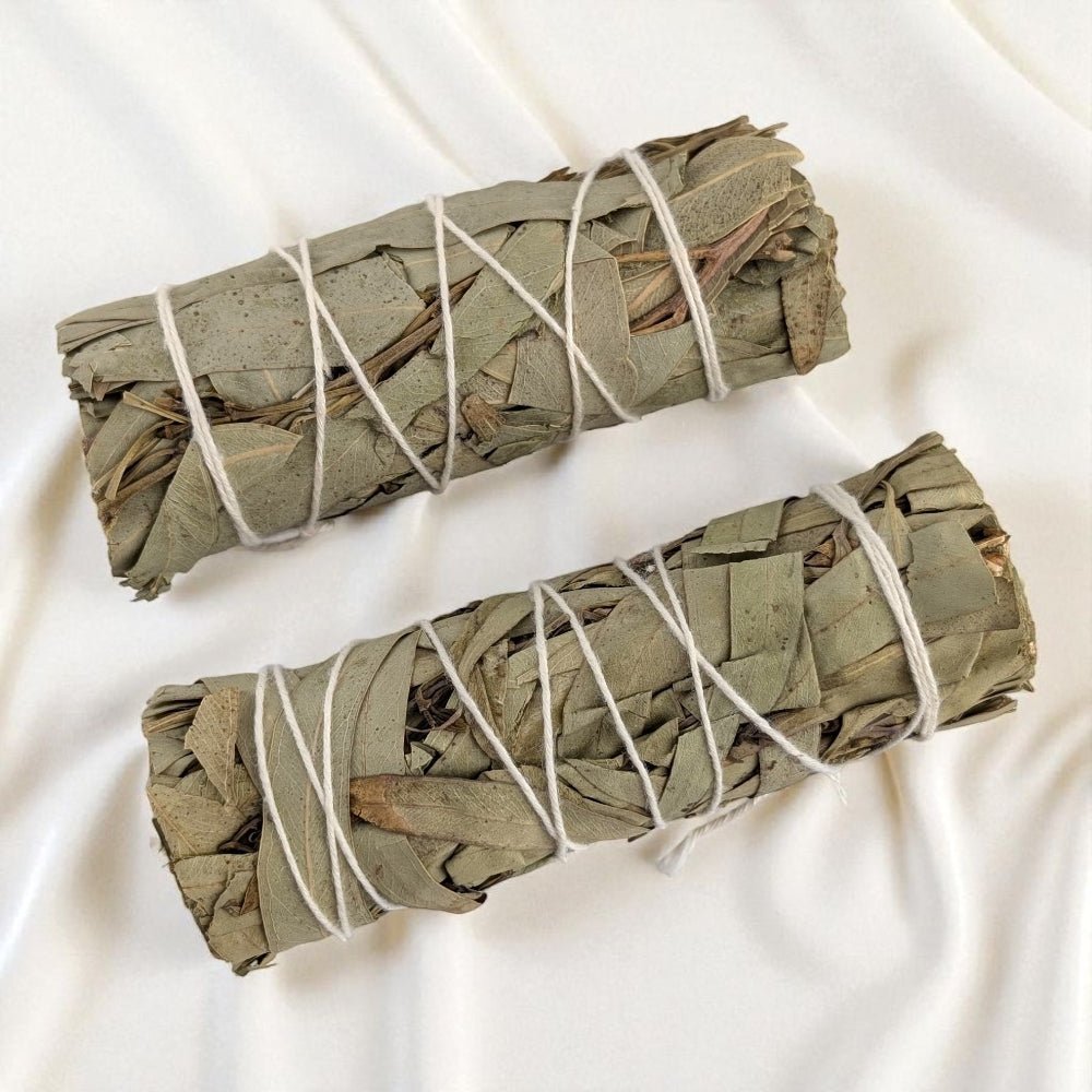 Two eucalyptus smudge sticks tied with white string on a white background sourced by metaphysical store Barrie