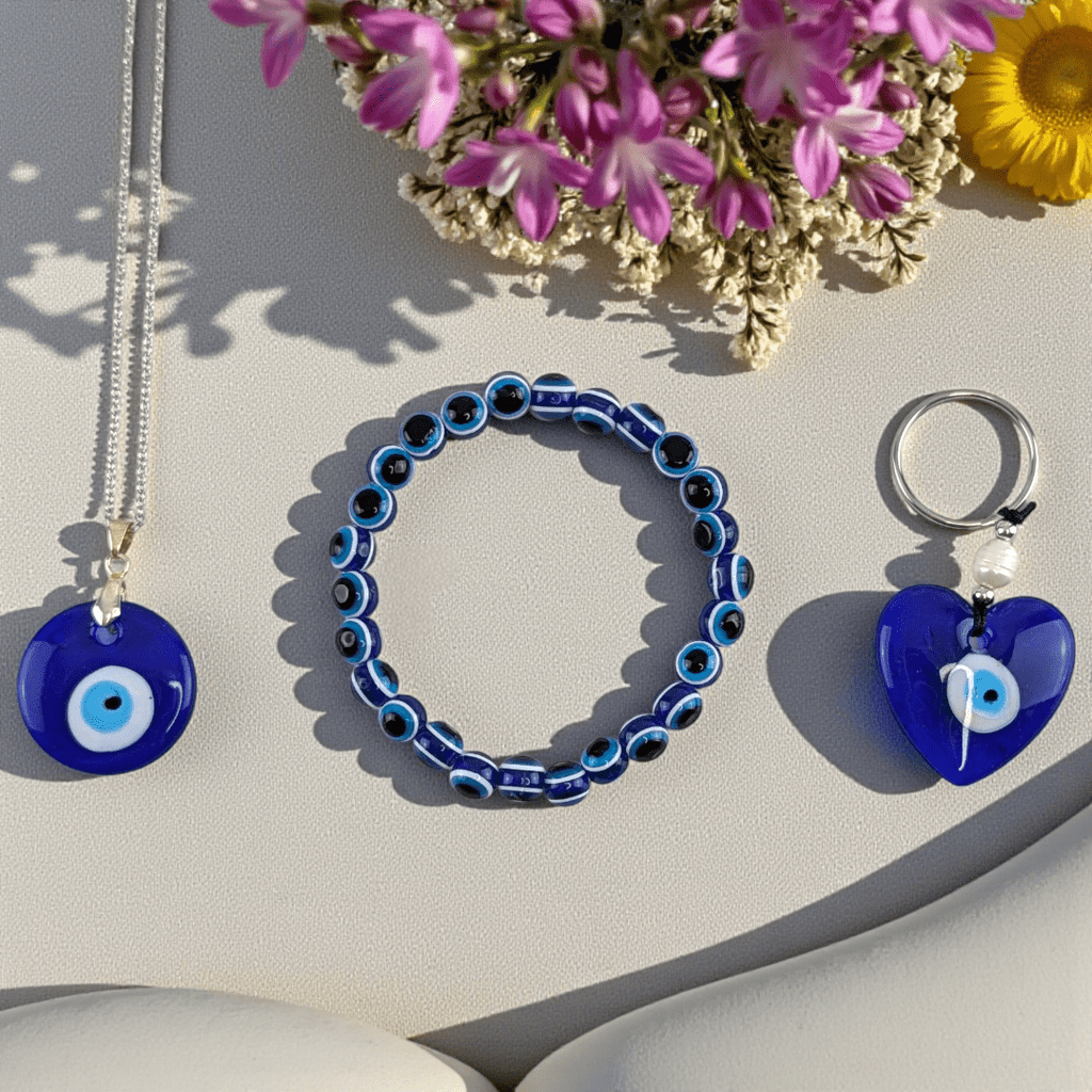 Blue evil eye jewelry set including a necklace, bracelet, and keychain on a light surface with flowers. Shop in-store now or online 24/7 at Zen Collection Metaphysical Stores Barrie