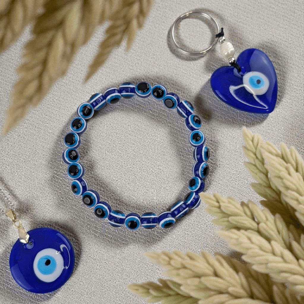 Blue evil eye jewelry set including a necklace, bracelet, and keychain on a light surface with flowers. Shop in-store now or online 24/7 at Zen Collection Metaphysical Stores Barrie