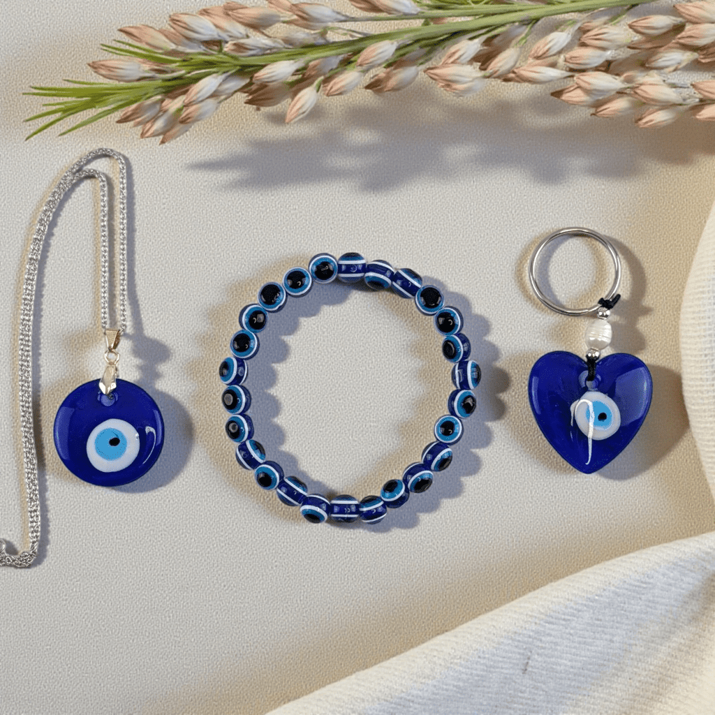 Blue evil eye jewelry set including a necklace, bracelet, and keychain on a light surface with flowers. Shop in-store now or online 24/7 at Zen Collection Metaphysical Stores Barrie