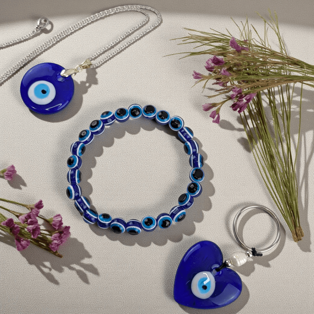 Blue evil eye jewelry set including a necklace, bracelet, and keychain on a light surface with flowers. Shop in-store now or online 24/7 at Zen Collection Metaphysical Stores Barrie