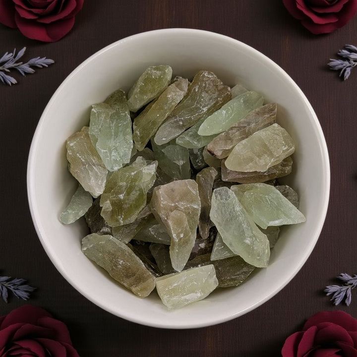 White bowl filled with green calcite crystal chunks on a dark surface with floral decorations. available at Zen Collection crystal healing store