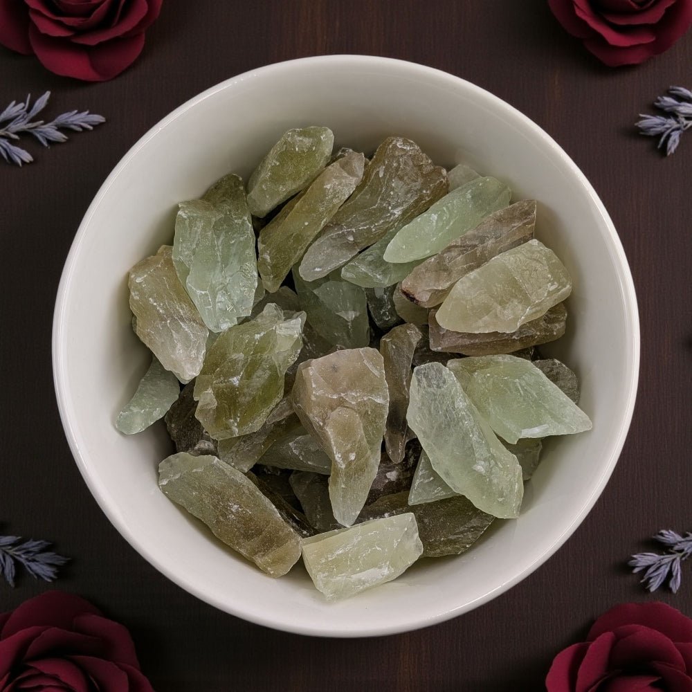 White bowl filled with green calcite crystal chunks on a dark surface with floral decorations. available at Zen Collection crystal healing store