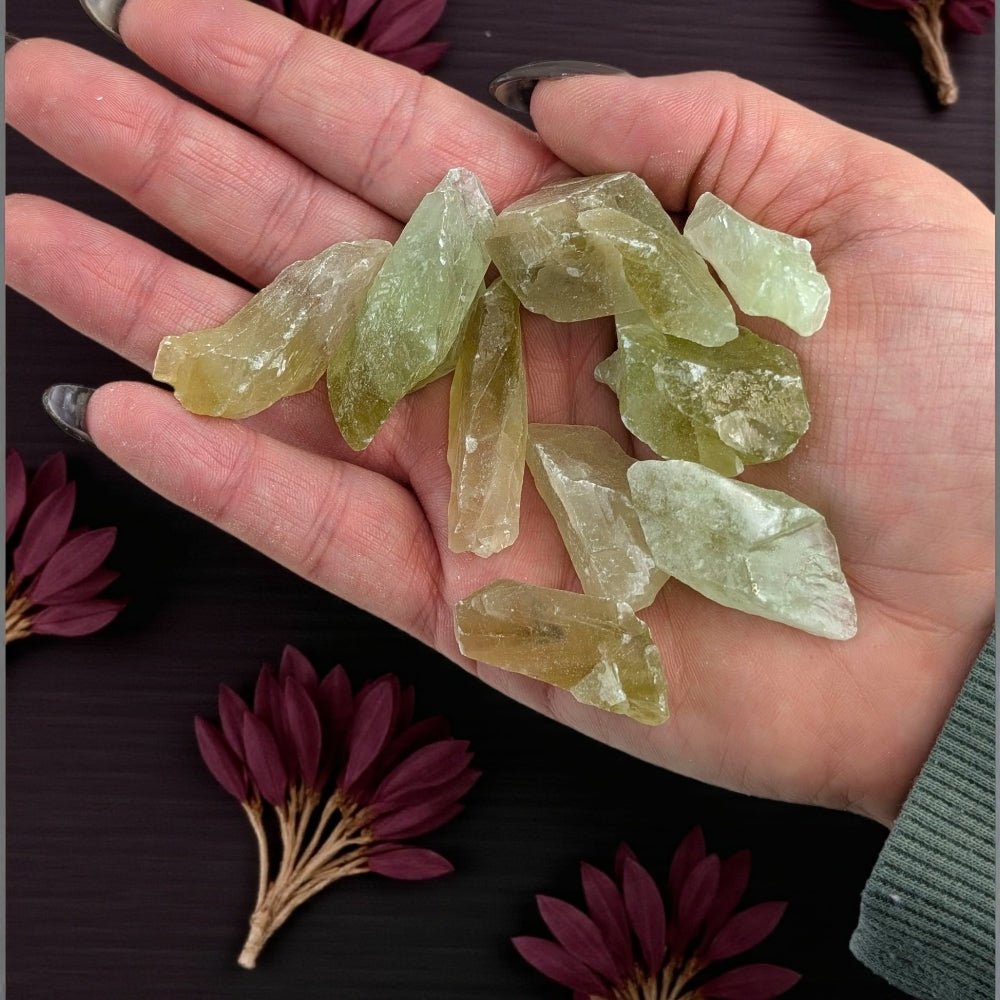 Heart Chakra Crystals - Hand holding green calcite crystal pieces with a dark background and purple flowers. available at zen collection crystal healing store