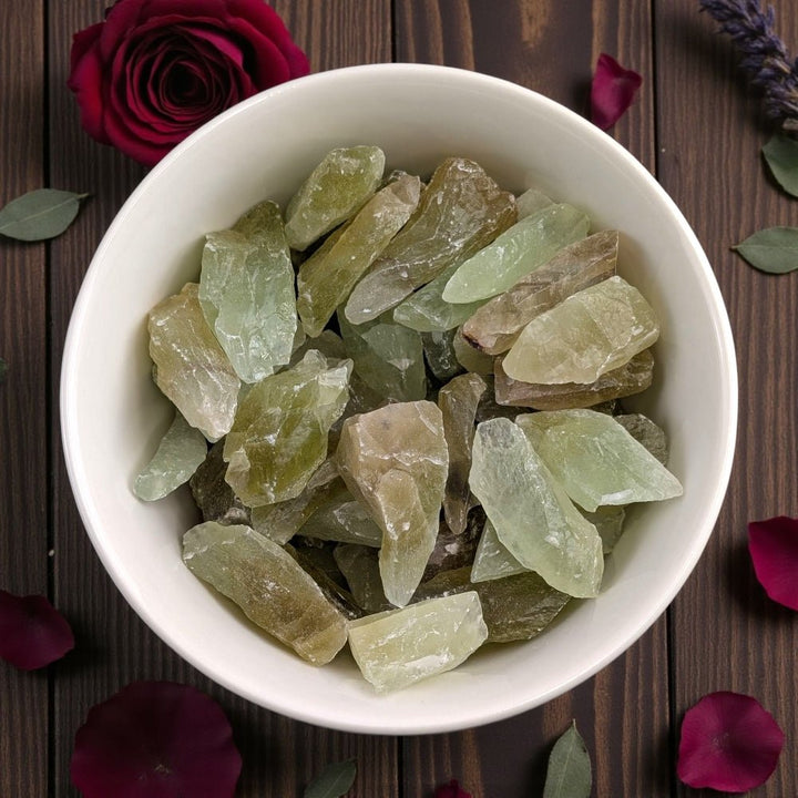 Heart Chakra Crystals - White bowl filled with green crystals on a wooden surface with flowers and leaves. Available at Zen Collection crystal healing store in barrie