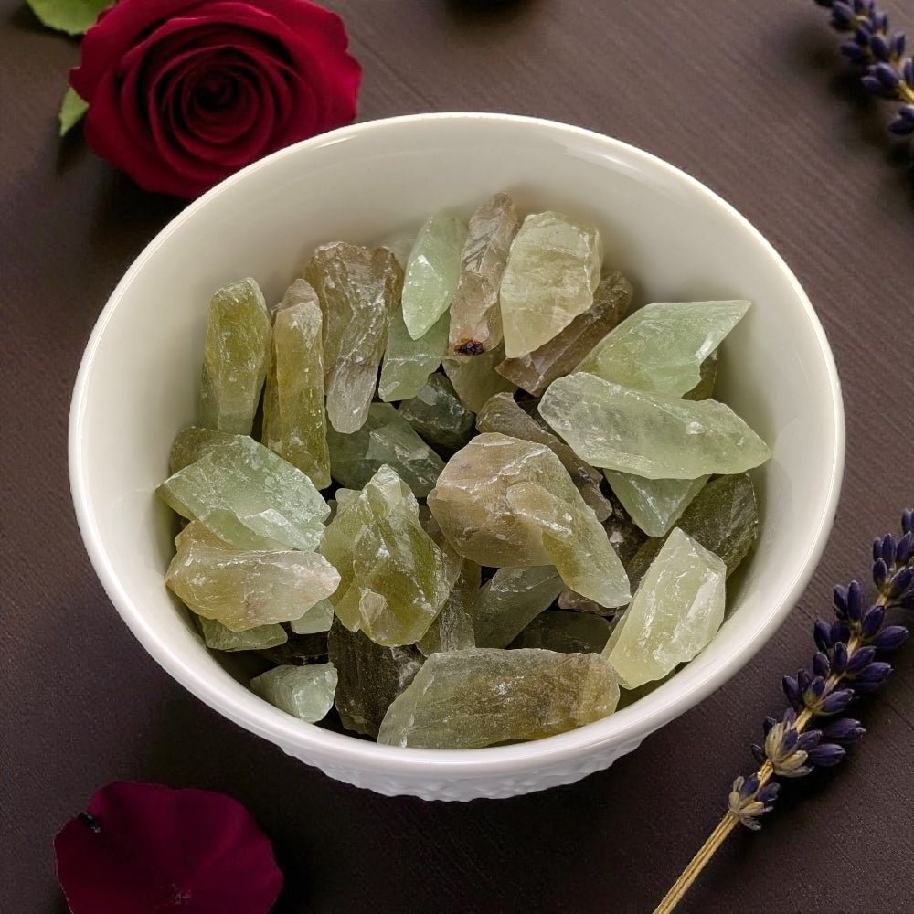 Heart Chakra Crystals - White bowl filled with green calcite crystals on a dark surface with flowers. available at zen collection crystal healing store