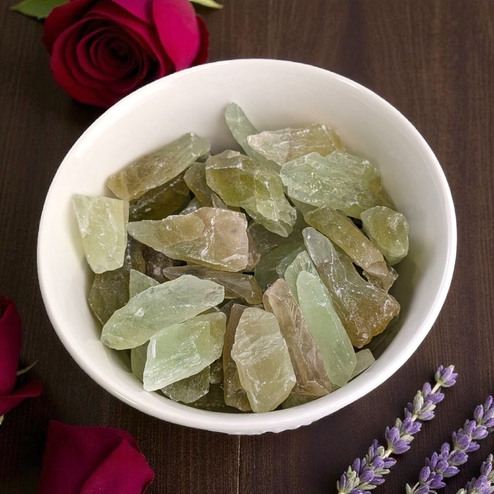 Heart Chakra Crystals - White bowl filled with green crystal-like stones on a wooden surface with flowers. Available at Zen Collection Crystal healing store in barrie 