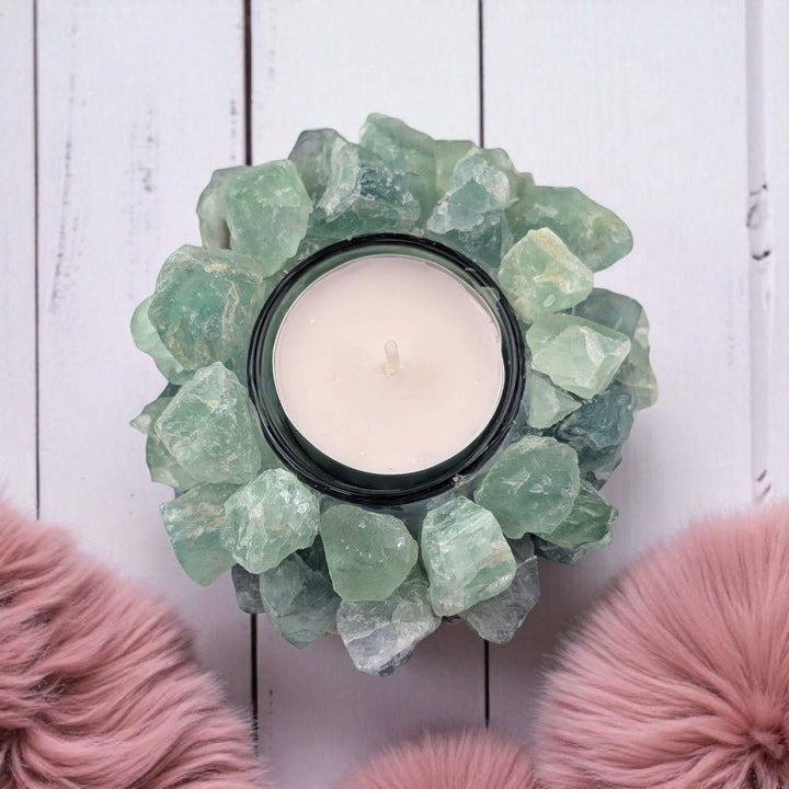 Candle holder made of green crystals on a white wooden surface with pink decorative elements.