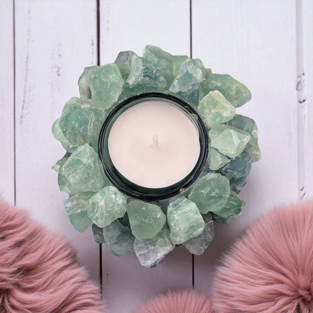 Candle holder made of green crystals on a white wooden surface with pink decorative elements.